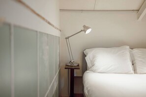 A bedroom with a bed, white bedding, a bedside table, and a desk lamp.