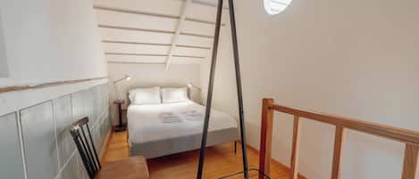 Un dormitorio con cama, una silla, una lámpara colgante y una ventana.