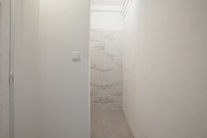 A narrow hallway with white walls and a marble-patterned shower area.