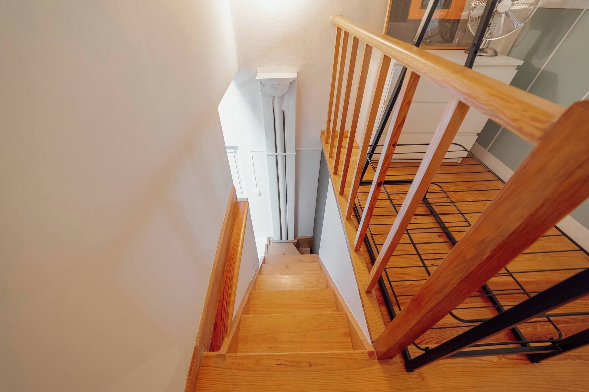A wooden staircase with a handrail, leading to a room with a white wall and a window.