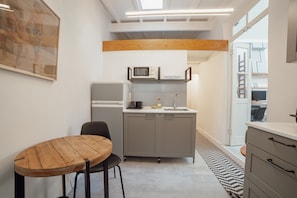 A compact kitchen with a microwave, sink, and cabinets, a wooden dining table with chairs, and a view into the adjacent room. - Clerigos Loft by Hosty (Oporto)