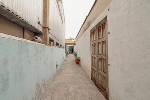 A narrow alleyway with a corrugated metal wall on the left and a wooden door on the right. There are potted plants along the alley.