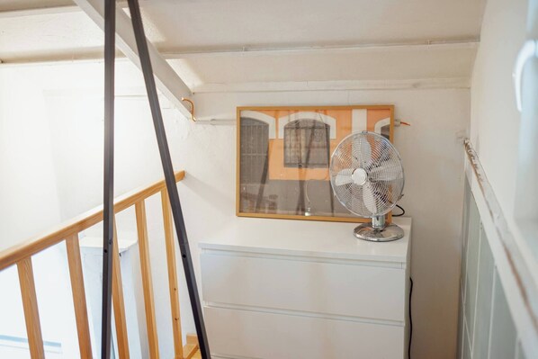 A room with a white dresser, a standing fan, and a framed picture on the wall.