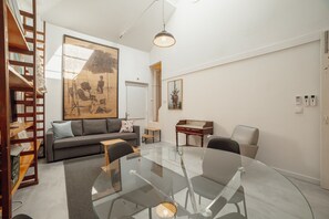 A modern living room with a glass table, grey sofa, and wooden shelving.