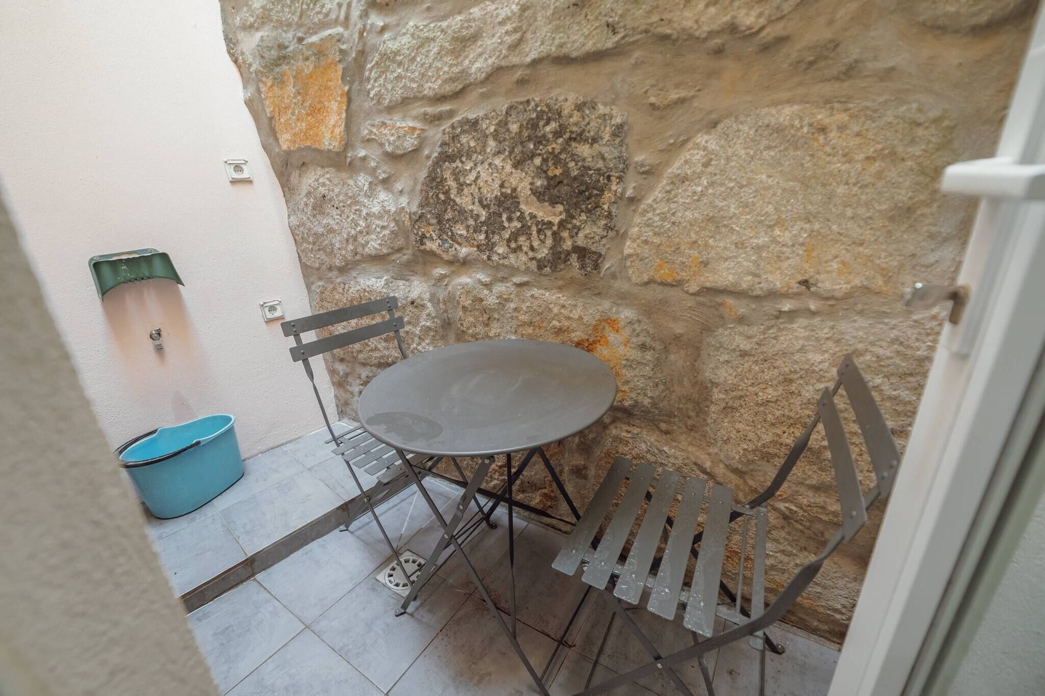 A stone wall, a metal table with chairs, and a blue bucket.