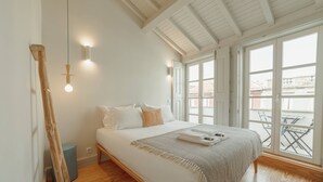 Ein Schlafzimmer mit einem Bett, Holzboden, einem großen Fenster und Blick ins Freie.