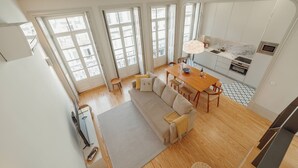Ein geräumiger Wohnbereich mit Sofa, Esstisch, Stühlen, großen Fenstern und einer Küchenzeile.