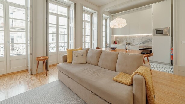 Ein modernes Wohnzimmer mit einer Couch, einem kleinen Holzschemel und einem Essbereich mit Tisch und Stühlen.