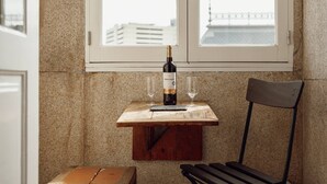 A wooden table with a bottle of wine and two glasses, positioned in front of a window with a view of buildings. - Downtown Bolhão 3 by Hosty (Porto)