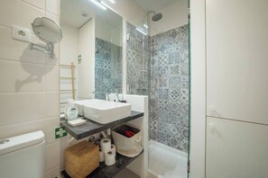 A bathroom with a white sink, mirror, and shower. There is a towel rack, a basket, and a shelf with toiletries.