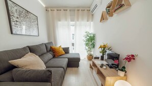 Un salon moderne avec un canapé d’angle gris, une table d’appoint en bois, un téléviseur à écran plat et une plante en pot.