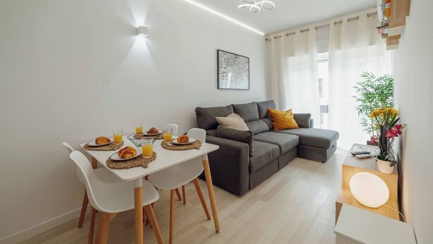 Un salon moderne avec un canapé gris, une table à manger avec des chaises et une petite table d’appoint agrémentée d’une plante.