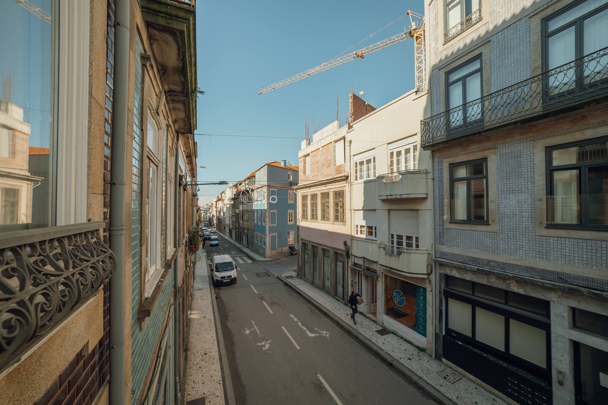 Een smalle straat met gebouwen aan beide kanten, een geparkeerde auto en een verre hijskraan.