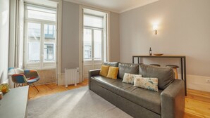Una sala de estar moderna con un sofá gris, dos ventanas, un radiador y una mesita con un cuenco.