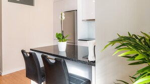 Een moderne keuken met een zwart aanrecht, een roestvrijstalen koelkast en twee zwarte stoelen.