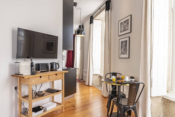 A compact kitchen with a microwave, toaster, and kettle on a wooden counter. There is a dining table with chairs and a hanging pendant light.