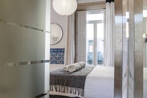 Een hotelkamer met een bed, een raam met gordijnen, een witte muur met blauw betegelde decoratie en een witte deur.