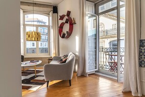 Un salon moderne avec un canapé gris, un tapis à motifs et une grande fenêtre donnant sur des immeubles.