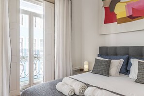Habitación de hotel con cama, mesita de noche, lámpara y vistas al balcón exterior.