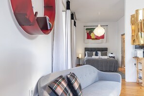 A modern hotel room with a grey sofa, a bed with grey bedding, a white wall with a painting, a hanging light fixture, and a wooden sideboard. - Mouzinho Penthouse by Hosty (Porto)