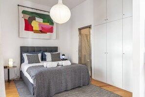 Ein modernes Schlafzimmer mit einem großen Bett, einem Nachttisch, einer Lampe, einem Kleiderschrank und einem Bild an der Wand.