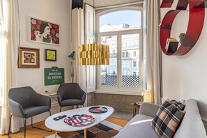 Ein modernes Wohnzimmer mit einer Couch, zwei Sesseln, einem Couchtisch und einem großen Fenster mit Blick auf Gebäude.