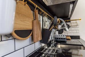 Une cuisine moderne avec des ustensiles en bois suspendus à un porte-ustensiles, un évier en acier inoxydable et un plan de travail noir.