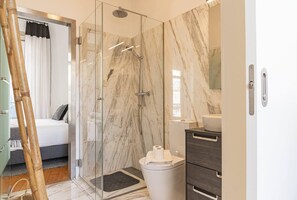 Een moderne badkamer met een glazen douchecabine, marmeren wanden en een houten vloer.