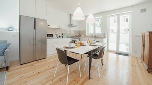 Une cuisine moderne avec des meubles blancs, des appareils en acier inoxydable et un coin repas comprenant une table et des chaises blanches.