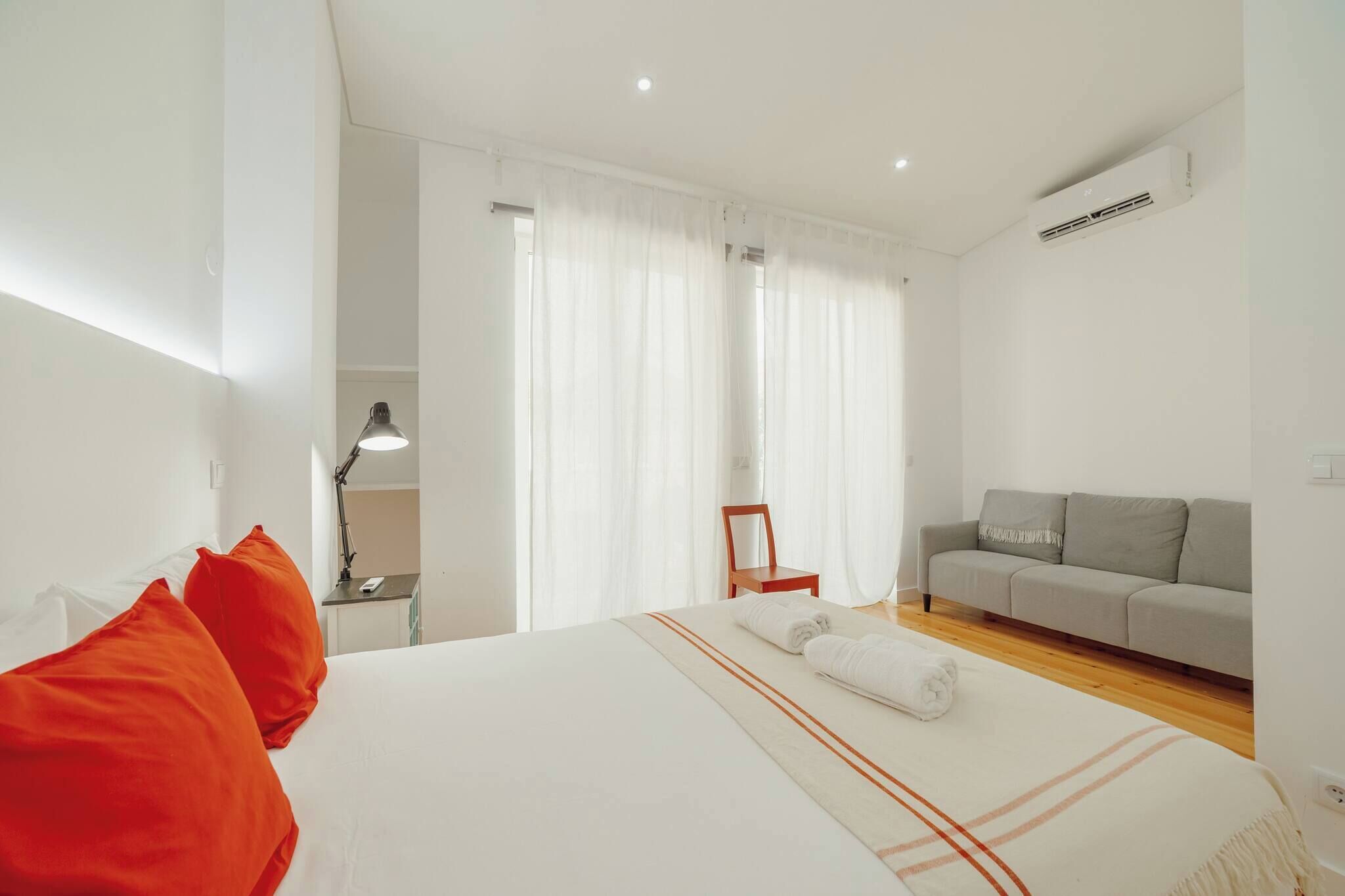Habitación de hotel con cama, sofá, sillón y escritorio con lámpara.
