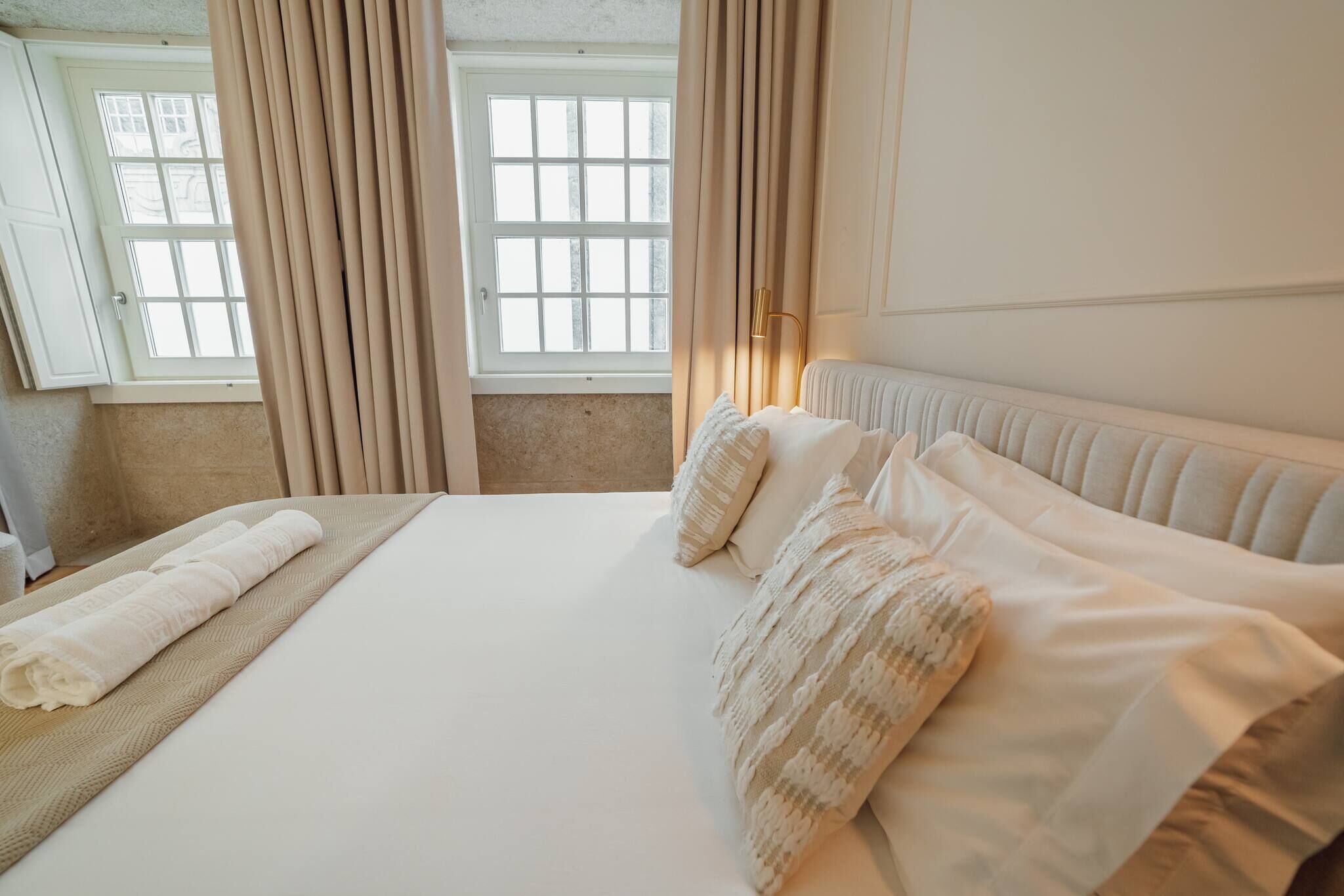Una habitación de hotel con una cama grande, cortinas color beige, un ventanal con vistas y un radiador.