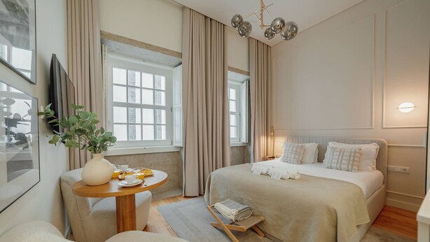Ein Schlafzimmer mit Bett, Nachttisch, Vorhängen, einer Pflanze und einem Fenster.