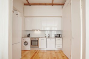 A compact kitchen with white cabinets, a washing machine, an oven, and a dishwasher. - Constituição Deluxe by Hosty (Oporto)