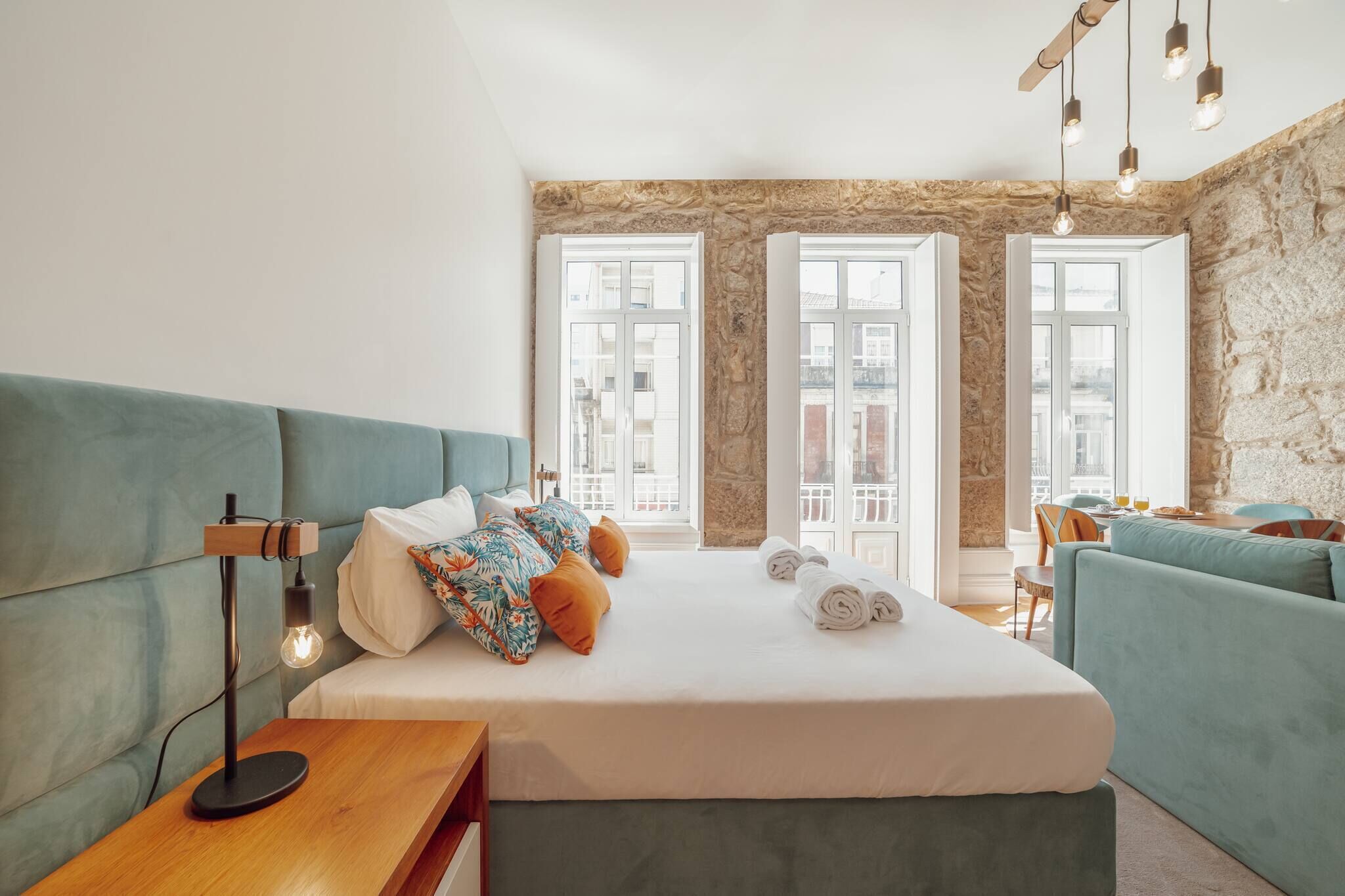 Una habitación de hotel moderna con una cama grande, un sofá, una mesita de noche de madera y una pared de piedra.