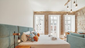 A modern hotel room with a large bed, a sofa, a wooden nightstand, and a stone wall. - Constituição Deluxe by Hosty (Oporto)