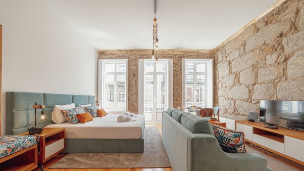 A modern room with a bed, sofa, TV, and stone wall. - Constituição Deluxe by Hosty (Oporto)