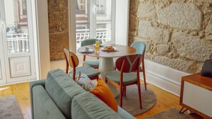 A dining area with a round table, chairs, and a view of buildings through large windows. - Constituição Deluxe by Hosty (Oporto)