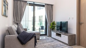 A modern living room with a sofa, a flat-screen TV, a potted plant, and a sliding glass door leading to an outdoor area. - Bloomfields Modern 2BR Azizi Gardens (Dubai)