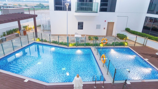 A swimming pool with a tiled deck, surrounded by a white building with large windows and a balcony. - Bloomfields Modern 2BR Azizi Gardens (Dubai)