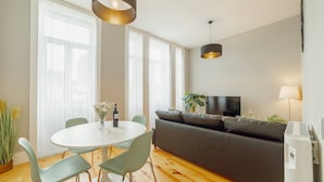 A modern living room with a round dining table, green chairs, a grey sofa, and a TV. - Bonfim Premium by Hosty (Porto)
