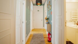 Ein Flur mit einem Feuerlöscher, einem gemusterten Teppich und einem an der Wand befestigten Regal mit einer Vase.