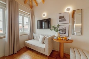 Une pièce comprenant un canapé, une table ronde avec des éléments pour le petit-déjeuner, un téléviseur et des tableaux encadrés au mur.