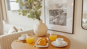 A breakfast table with a croissant, orange juice, and a vase with green leaves.