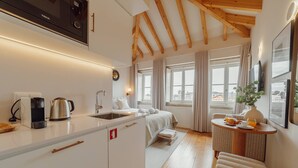 A compact hotel room with a kitchenette, a bed, a small dining table, and a window with a city view.