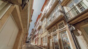 A narrow cobblestone street lined with multi-story buildings, featuring balconies and traditional European architecture.
