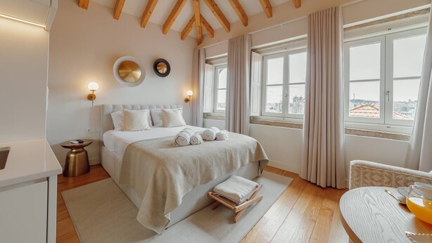 A bedroom with a bed, bedside tables, a view through large windows, and wooden beams on the ceiling.
