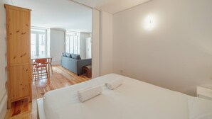 Un dormitorio con cama, armario de madera, escritorio con sillas y un sofá al fondo.