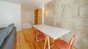 Una habitación con una mesa blanca, sillas anaranjadas, un sofá gris y una pared de piedra.