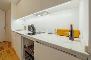 Una cocina moderna con armarios blancos, lavavajillas integrado, una encimera con una botella de vino y un electrodoméstico amarillo.