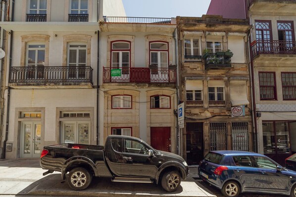 A multi-story building with a parking sign, a pickup truck, and a blue car parked on the street. - Cozy Almada by Hosty (Oporto)